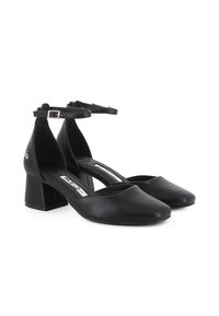 Tacones de bloque negros de cuero con puntera cerrada, correas en el tobillo y hebillas plateadas, exhibidos sobre un fondo blanco.