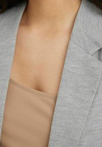 Szary, teksturowany kołnierz marynarki w połączeniu z dopasowanym beżowym topem. Materiał ma subtelny wzór z czystymi liniami w designie.