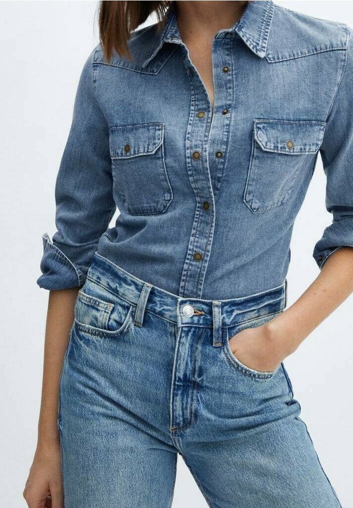 Chemise en denim avec fermeture boutonnée à l'avant, poches poitrine et manches retroussées. Associée à un jean en denim taille haute présentant un lavage bleu classique.