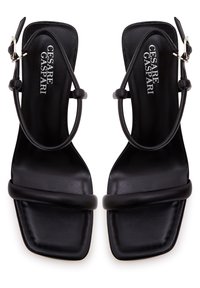 Sandalias de tacón de cuero negro con punta cuadrada, tiras delgadas y hebilla en el tobillo. En el interior se muestra el nombre de la marca en texto plateado.