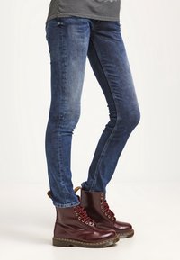 Skinny jeans in dark blue denim paired with burgundy lace-up ankle boots, featuring a smooth finish and contrasting stitching details.