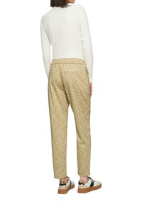 Beige gemusterde tapse broek met een elastische tailleband, gecombineerd met een witte lange mouw top en sneakers met zwarte accenten.
