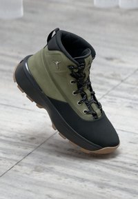 Green and black hiking boot with a textured upper, padded collar, and rubber sole. Features black laces and logo detail on the side.