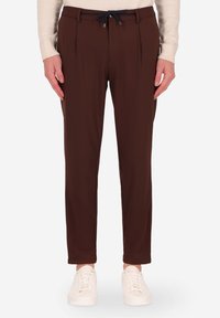 Pantaloni marroni a vita alta con pinces, caratterizzati da una vita con cordoncino, tessuto liscio e gambe affusolate, indossati con sneaker bianche.