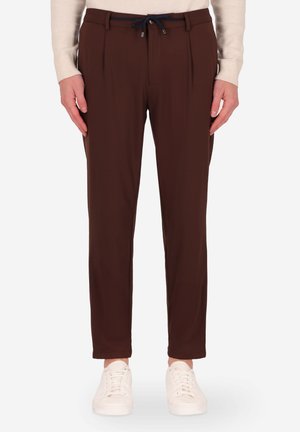 Pantaloni marroni a vita alta con pinces, caratterizzati da una vita con cordoncino, tessuto liscio e gambe affusolate, indossati con sneaker bianche.