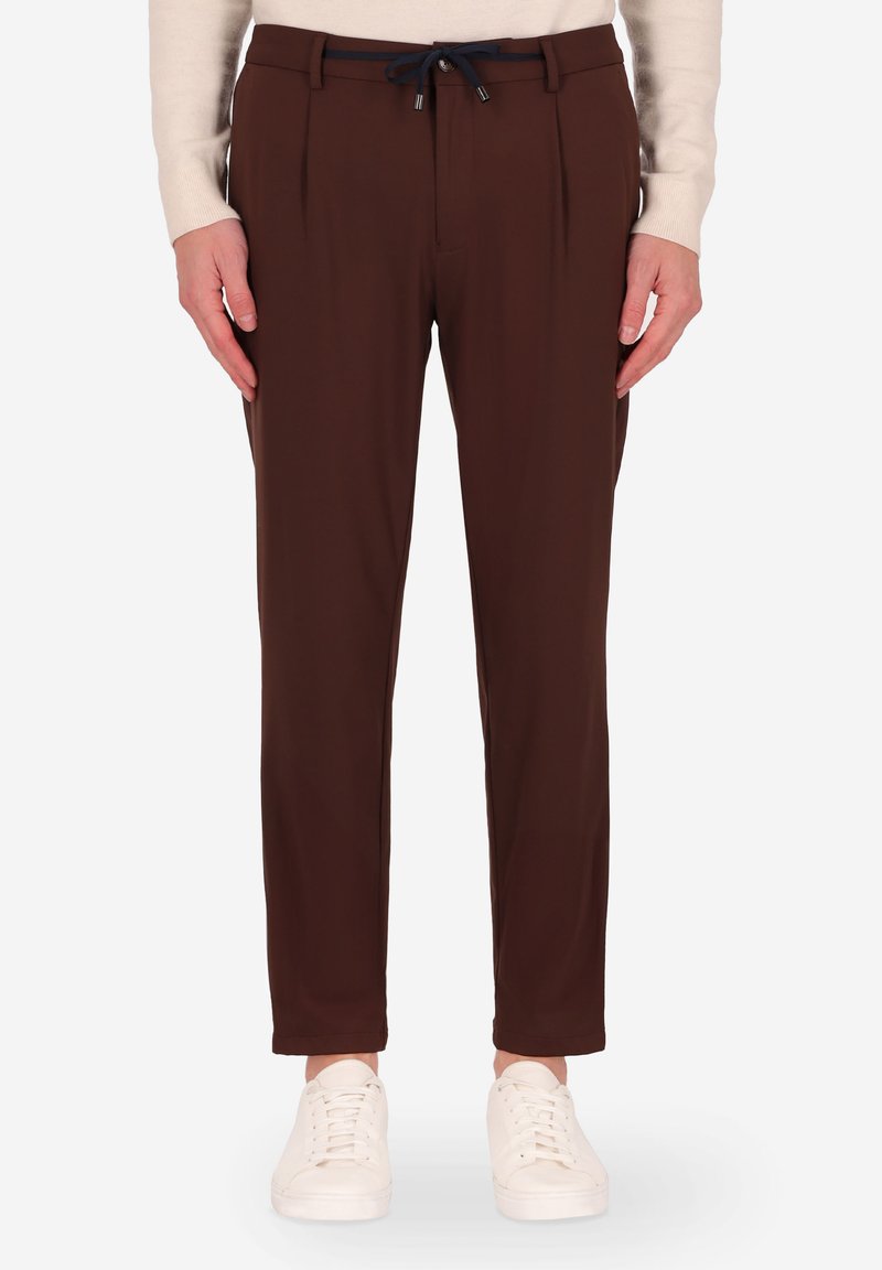 Pantaloni marroni a vita alta con pinces, caratterizzati da una vita con cordoncino, tessuto liscio e gambe affusolate, indossati con sneaker bianche.