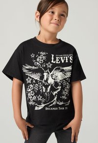 Noor laps wearing black Levi's t-särk, millel on tiivuline hobune, tähed ja lillemotiivid koos tekstiga "Dreamer Tour 73'".