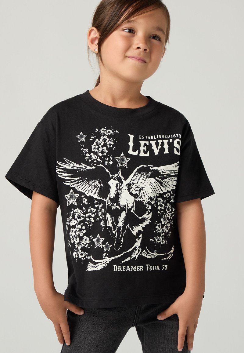 Noor laps wearing black Levi's t-särk, millel on tiivuline hobune, tähed ja lillemotiivid koos tekstiga "Dreamer Tour 73'".