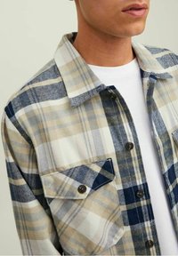 Chemise à carreaux présentant des couleurs beige, bleu et blanc ; en coton, avec un design à boutons sur le devant ; détail de poche poitrine avec rabat.