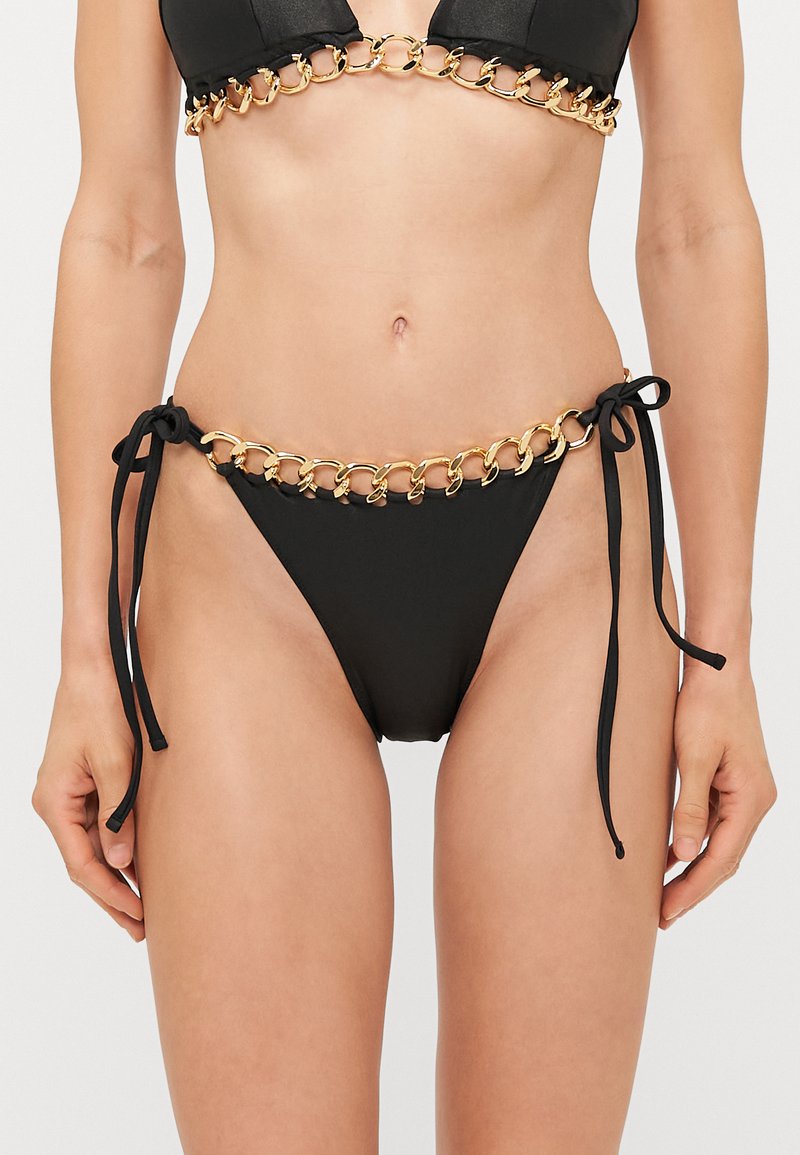 Melna bikini komplekts ar zelta ķēdes detaļu augšpusē un apakšpusē. Bikīni apakšdaļai ir regulējami saitītes un gluda auduma tekstūra.
