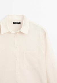 Lysbeige skjorte med knapper, lavet af blødt stof, med en foldet krave, frontlomme og glat overflade. Brandmærket er synligt.