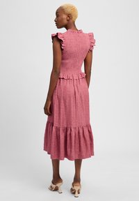 Roze textuur jurk met gedrapeerde mouwen en een gelaagde zoom, met een getailleerde lijfje en ritssluiting aan de achterkant. Soepele stofafwerking.