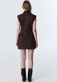 Braunes ärmelloses Kleid mit einer Kunstwildleder-Textur und strukturiertem Kragen, das eine taillierte Passform und eine Länge bis zur Mitte des Oberschenkels bietet. Schwarze knielange Stiefel.