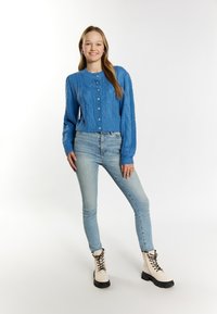 Suéter azul de punto con cuello redondo y cierre de botones, combinado con jeans de mezclilla claros y botas de ante beige con cordones y suelas negras.