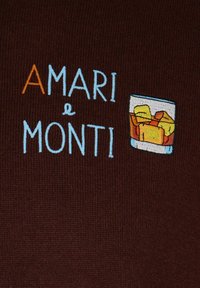 Dunkelbrauner Stoff mit gesticktem Text "AMARI & MONTI" und einem bunten Glas mit Eiswürfeln und Flüssigkeit auf der rechten Seite.