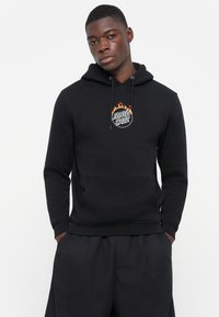 Zwarte hoodie met een buidelzak en een rond logo met vlammen, gemaakt van zacht materiaal met een comfortabele pasvorm.