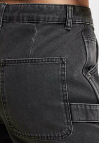 Black denim jeans featuring a back pocket, visible stitching, and a smooth texture. The waistband is slightly tapered at the top.