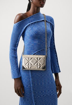 Metalen zilveren schoudertas met doorgestikt diamantenpatroon, zilveren kettingriem, gecombineerd met een textuurrijk blauw geribd jurkje met een off-shoulder ontwerp.