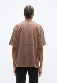 Καφέ βαμβακ ερό κοντομάνικο μπλουζάκι, με απλό σχέδιο και εκτυπωμένο λογότυπο στην πλάτη, εμφανιζόμενο από πίσω.