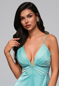 Aqua Satin-Kleid mit tiefem V-Ausschnitt, Raffung an der Taille und dünnen Trägern. Das Modell kombiniert es mit blumigen Ohrringen und einem Armband.
