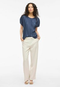 Mornarska bluza s kratkimi rokavi in plisiranim dizajnom z okroglim izrezom, v kombinaciji z kremnimi širokimi hlačami in svetlimi sandali. Preprost, eleganten dizajn.