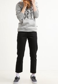Sudadera gris con capucha y diseño geométrico negro, combinada con pantalones negros recortados y zapatillas grises, sobre un fondo liso.
