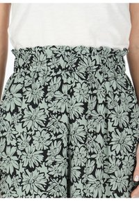 Gonna midi floreale in verde chiaro e nero. Presenta una vita arricciata e un motivo floreale su tutta la superficie con fiori di forme e dimensioni diverse.