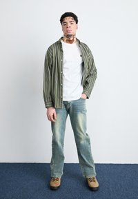 Grøn- og hvidstribet skjorte med knapper over en hvid t-shirt, parret med lyseblå denimjeans og brune snørebåndsstøvler.