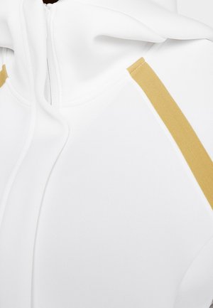 Nahaufnahme eines weißen Kapuzenpullovers mit Reißverschluss vorne und goldfarbener, diagonaler Streifendetail am Schulterbereich.