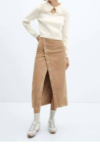 Suéter de punto color crema con un cuello decorativo, combinado con una falda de pana beige hasta la rodilla, que cuenta con una tapeta de botones en la parte frontal y una abertura.