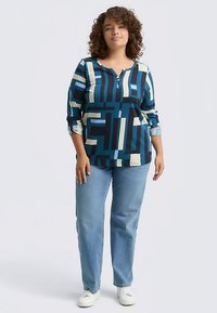 Večbarvna dolga majica z geometrijskimi vzorci v modri, črni in kremni barvi. Ima okrogel izrez in gumb na sprednji strani.