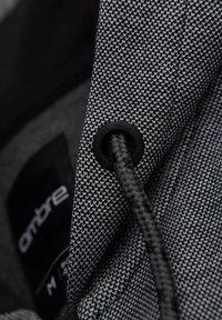 Un tejido a rayas en blanco y negro presenta un cordón con un tope de plástico negro. Etiqueta visible con el nombre de la marca "ombre" en blanco.