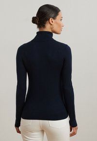 Marinefarbener Rollkragenpullover in einer taillierten Passform, aus glattem Material mit langen Ärmeln und einem gerippten Kragen, kombiniert mit weißen Hosen.