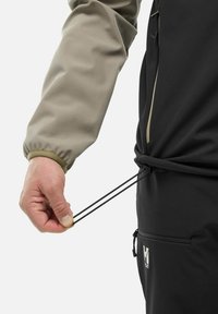 Vêtements d'extérieur noir et gris avec ajustement à la taille par cordon de serrage. Main tenant une corde noire, montrant la flexibilité du tissu et les détails de conception.