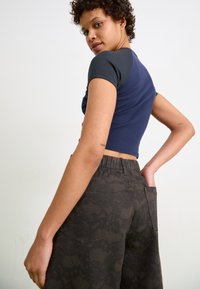 Marineblå ribbet crop top med korte grå ærmer, parret med mørkt mønstrede vide bukser med lommer og elastisk talje.