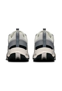 Zapatillas deportivas en gris y blanco con una parte superior de malla, amortiguación prominente y acentos en negro contrastante; suela de goma texturizada para mayor agarre.