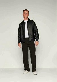 Black leather bomber jacket with ribbed cuffs, worn over a white t-shirt and black trousers, completed with white sneakers.