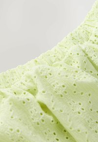 Tissu en coton vert clair avec une surface texturée, présentant des motifs de dentelle complexes et une taille élastique froncée.