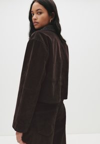 Rjava kordurojska skrajšana jakna s dokazanimi ovratnikom, sproščenega kroja in vidnim šivom. Gladka tekstura in stranske žepke.