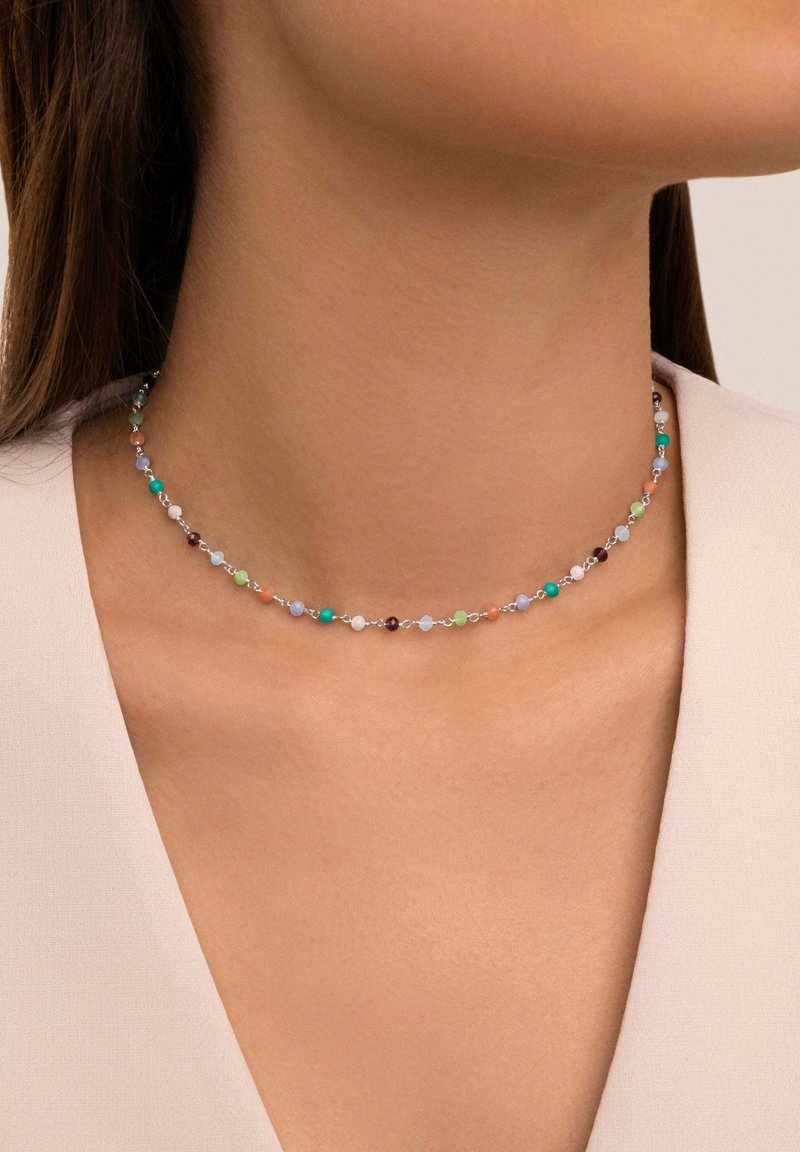 Collier ras-du-cou délicat avec petites perles rondes multicolores porté autour du cou d'une femme avec un haut beige clair.