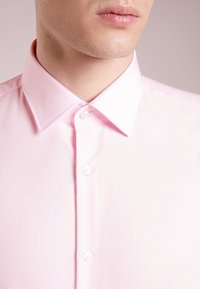 Lichtroze button-up shirt met een klassieke kraag en witte knoopdetails, gemaakt van een gladde stof met een gepolijste textuur.