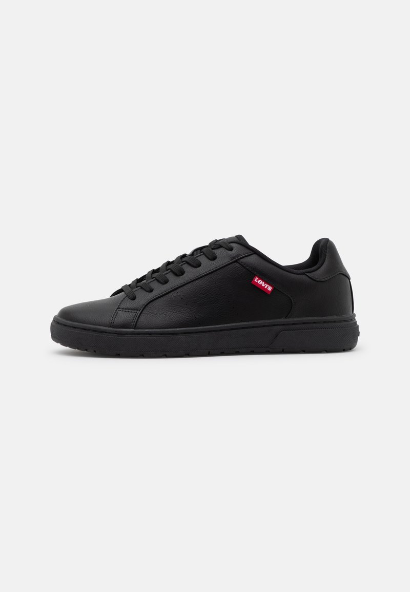  svarte sneakers laget av teksturert syntetisk materiale. Har rund tå, flat snøring og en liten rød logo på siden.
