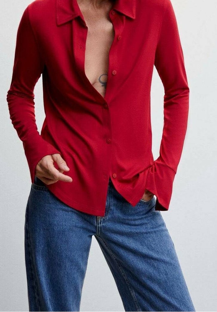 Chemise rouge à manches longues à boutons avec col, présentant un décolleté en V profond, en tissu doux, et une coupe décontractée, associée à un jean en denim bleu.