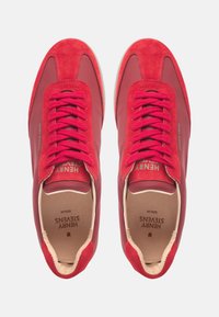 Rote Sneaker aus einer Kombination von Wildleder und strukturiertem Material, mit flachen Schnürsenkeln, einer gepolsterten Innensohle und Branding auf der Zunge und den Seiten.