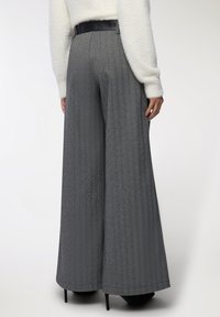 Osoba w szarych spodni o wysokim stanie i szerokich nogawkach w jodełkę, z czarnym skórzanym paskiem i czarnych szpilkach.