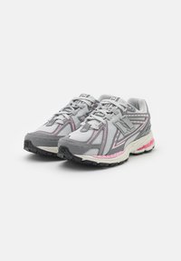 Un paio di scarpe da corsa New Balance grigie e rosa con lacci bianchi, realizzate in tessuto a rete e suole in gomma su sfondo bianco.
