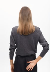 Grauer Strickpullover mit langen Ärmeln, enganliegenden Bündchen und einer lockeren Silhouette, von hinten gesehen, kombiniert mit dunklen Hosen.