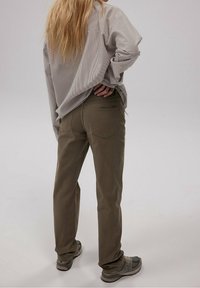 Pantalons vert olive en tissu léger, présentant une coupe droite et des poches arrière, associés à une chemise beige à rayures ample.