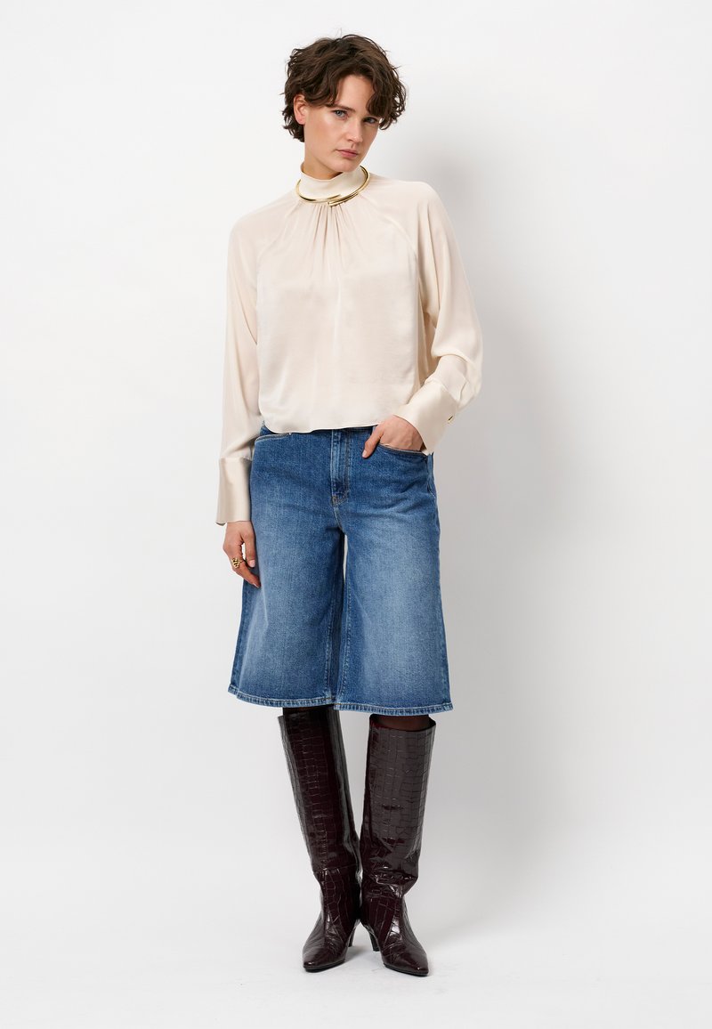 Silky cream blouse with gathered neckline, paired with blue denim culottes and glossy burgundy knee-high boots with a crocodile pattern.