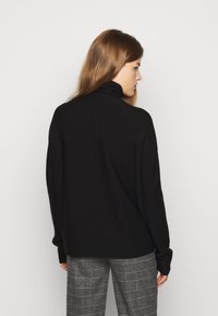 Pulover negru cu guler înalt, cu o croială lejeră, având mâneci lungi și o textură moale. Asortat cu pantaloni gri în carouri.